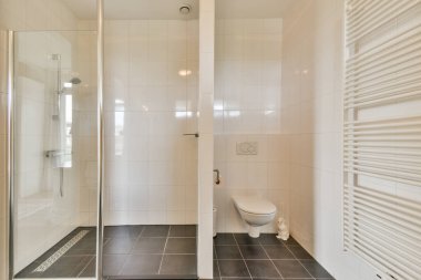 Pürüzsüz ve çağdaş bir banyo. Cam duş, tuvalet ve minimalist tasarım. Beyaz fayanslar ve koyu döşemeler..