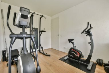 Şık, minimalist, ahşap döşemeli ve nötr duvarlı spor salonu ortamında çeşitli fitness makineleri sergileniyor..