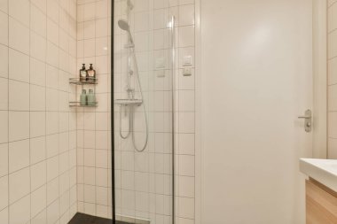 Parlak ve çağdaş bir duş odası, cam bir muhafaza, minimalist tasarım, ve temiz, ferah bir his için açık renkli fayanslar.