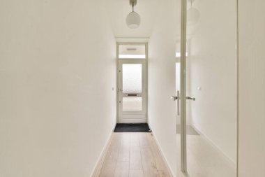 Beyaz duvarlar, ahşap döşemeler ve doğal ışığın boşlukları genişletmesine izin veren cam bir kapının bulunduğu parlak, minimalist bir koridor..