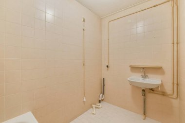 Temiz, minimalist bir banyo pembe fayanslı duvarlar ve basit bir lavabo düzeneği. Uzay modern ama az gösterilen bir estetik tasarımı yansıtıyor..