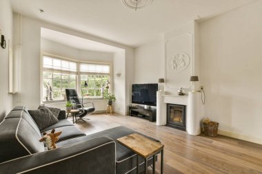 Rahat bir kanepe, şık bir şömine ve geniş pencereli modern bir oturma odası. Parlak ve davetkar bir atmosfer yaratıyor..