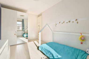 Yumuşak mavi yatak odaları, minimalist tasarımı ve açık renkli duvarları olan, parlak ve davetkar bir atmosfer yaratan rahat ve modern bir çocuk odası..