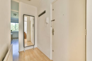 Geniş bir ayna, ceket kancaları ve yaşam alanına bakan manzaralı parlak ve havadar bir giriş. Ahşap zemin minimalist estetiği tamamlıyor..