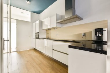 Beyaz dolaplar, siyah tezgah ve temiz çizgiler içeren gösterişli, modern bir mutfak. Tasarım uzayda basitlik ve işlevselliği vurgular.