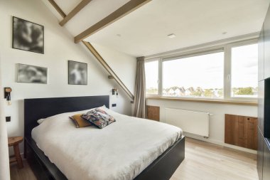 Rahat bir yatak odası, dekoratif yastıklar ve geniş pencereli geniş doğal ışık sağlayan bir yatak odası. Minimalist tasarım gevşemeyi arttırır.