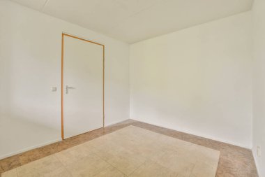 Beyaz duvarları ve basit bir kapısı olan ferah bir iç mekan. Zeminin bej bir dokusu var, temiz ve modern bir atmosfer yaratıyor..