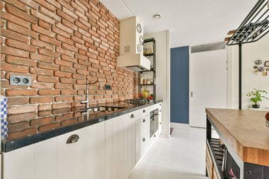 Açığa çıkmış tuğla duvarlar, gösterişli dolaplar ve minimalist dekorlarla donatılmış modern bir mutfak. Tasarım, rustik ve çağdaş estetiğin bir karışımını sunuyor..