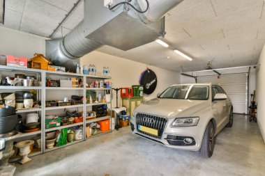 Rafların yanına park edilmiş gümüş renkli bir SUV 'u gösteren iyi ışıklandırılmış bir garaj. Çeşitli organize araç ve gereçleri barındırıyor. İşlevselliği ve boşluğu vurguluyor..