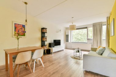 İçinde ahşap bir yemek masası, şık sandalyeler, bir kitaplık ve büyük pencereler ve zevkli bir dekorun yarattığı parlak bir ortam olan rahat bir oturma odası..