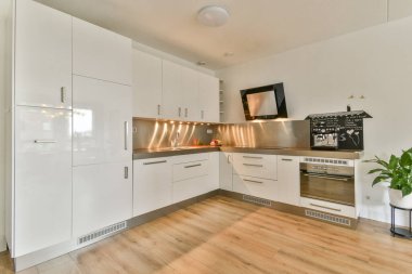 İçinde minimalist dolaplar, paslanmaz çelik eşyalar ve sıcak ahşap zemin bulunan çağdaş bir mutfak. Modern yaşam alanları için ideal, işlevselliği stille harmanlamak.