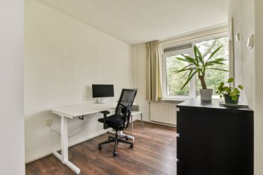 Masa, sandalye ve bitkilerin yer aldığı parlak ve minimalist bir ev ofisi. Büyük pencereler doğal ışığa izin verir, ilham verici bir çalışma alanı oluşturur.