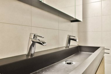 Zarif banyo lavabosu ve çağdaş musluklarla döşenmiş duvarlara dayalı minimalist tasarım, şık ve temiz bir estetik sergileniyor..