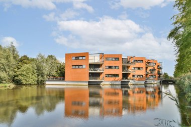 Su kenarında çarpıcı bir modern bina, berrak çizgiler ve eşsiz bir tasarım sergiliyor. Sudaki yansıma, doğal yeşilliğin ortasında güzelliğini artırır..