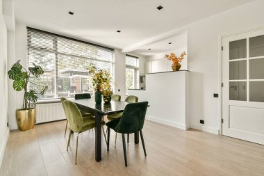 Modern bir masası, şık sandalyeleri ve davetkar bir atmosfer yaratan canlı bitkileri olan gösterişli, parlak bir yemek alanı. Doğal ışık, temiz tasarım elementlerini geliştirir.