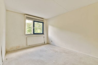 Doğal ışığın mekanı aydınlatmasına izin veren penceresi olan temiz ve boş bir oda. Duvarlar sade, minimalist bir estetik oluşturuyor..