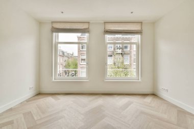 Doğal ışığın içeri akmasına izin veren, nötr renk paleti ve ahşap döşemeleri gösteren geniş pencereli minimalist bir iç mekan..