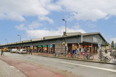 Çeşitli mağazaların, açık hava oturma yerlerinin ve temiz mavi gökyüzünün altında asfalt bir cadde boyunca park edilmiş bisikletlerin bulunduğu hareketli modern bir alışveriş alanı..