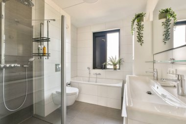 Zarif demirbaş, cam duş ve saksı bitkilerinin bulunduğu modern bir banyo huzur ve çağdaş bir atmosfer yaratıyor..
