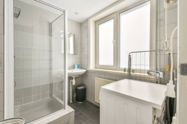 Cam duş, çamaşır makinesi ve doğal ışığın mekanı aydınlatmasına izin veren parlak bir pencerenin yer aldığı gösterişli, çağdaş bir banyo..