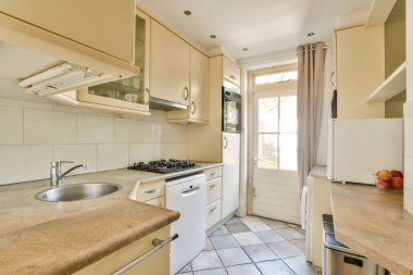 Parlak ve ferah mutfak, modern aletler, bej dolaplar, ve pencereden gelen doğal ışıkla güçlendirilmiş hoş geldin atmosferi..