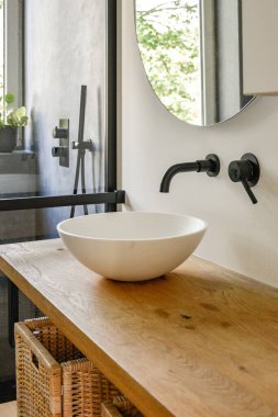 Şık ahşap bir tezgahın olduğu sakin bir banyo, modern bir lavabo ve doğal ışık sağlayan büyük pencereler, minimalist tasarımı geliştiriyor..