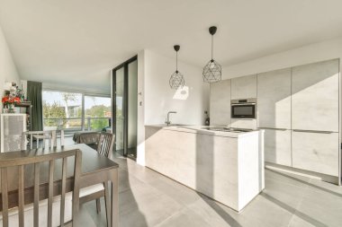 Açık renkli, zarif mobilyalı ve geniş pencereli minimalist bir tasarımı olan gösterişli bir modern mutfak, doğal ışığın mekanı aydınlatmasına olanak sağlıyor..