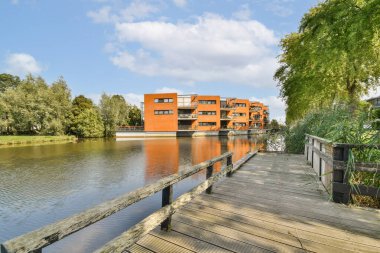 Şık, modern bir apartman kompleksi, berrak mavi gökyüzünün altında yemyeşil sularla çevrili sakin bir nehrin yanında oturur. Suyun kenarında yaşamak için ideal..