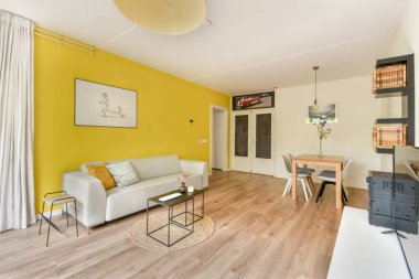 Parlak sarı duvarlar şık mobilyaları tamamlıyor, bu modern yaşam alanında samimi ve davetkar bir atmosfer yaratıyor. Misafirleri rahatlatmak ya da eğlendirmek için ideal.