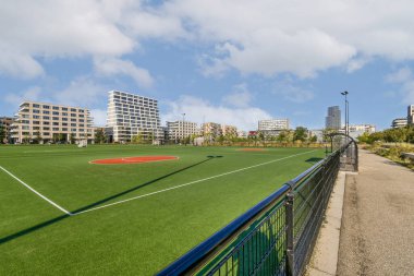 Çağdaş binalar ve yeşil alanlarla çevrili, boş zaman ve eğlence için ideal, bakımlı bir spor sahasının bulunduğu canlı bir şehir parkı..