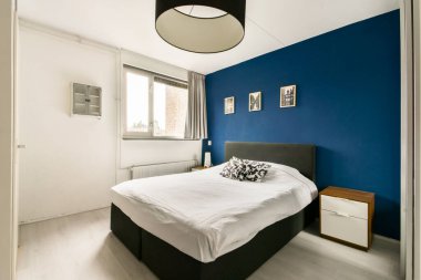 Sade ama zarif bir yatak odası, rahat bir yatak odası, minimalist bir dekor ve çarpıcı bir mavi aksan duvarı. Modern yaşam alanları için mükemmel..