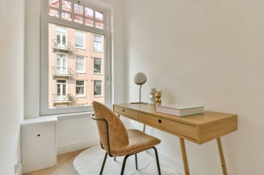 Ahşap bir masa, şık bir sandalye ve geniş bir pencereden bol miktarda doğal ışık içeren rahat bir çalışma alanı. Ev idaresi ilhamı ve modern estetik için ideal..