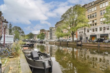 Amsterdam 'da canlı şehir yaşamını ve mimari güzelliği gözler önüne seren yemyeşil ağaçlarla çevrili bir kanal manzarası..