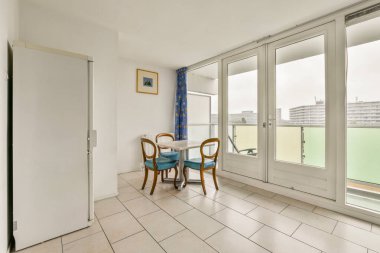 Küçük bir masa, sandalyeler, geniş pencereler, doğal ışık ve temiz estetik içeren parlak ve havadar bir minimalist yemek alanı..