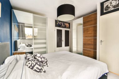 Mavi aksanlı duvarı, şık mobilyaları ve organize deposu olan modern bir yatak odası. Oda konfor ve çağdaş tasarım unsurlarının bir karışımını sergiliyor..