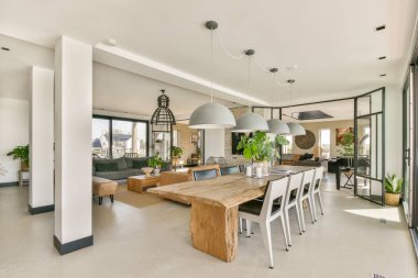 Geniş bir yemek masası, şık bir ışıklandırma ve yeşil bitkilerin yer aldığı parlak ve ferah bir açık konsept yaşam alanı. Çağdaş yaşam ve sosyal toplantılar için ideal.