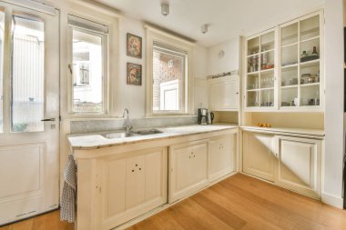 Modern tasarım eğilimlerini yansıtan, mermer tezgah, cam dolaplar ve doğal ışık içeren şık, parlak bir mutfak..