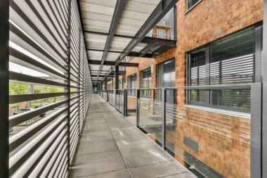 Çağdaş tasarım elementlerinin karışımından oluşan uzun bir koridor, cam korkuluklar ve tuğla duvarlar, doğal ışığı davet eden ve açıklık hissi veren..