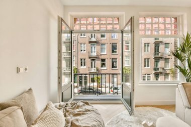 Doğal ışığın mekanı aydınlatmasına izin veren, rahat bir atmosfer ve şehir manzarası sunan açık pencereli modern bir oturma odası..