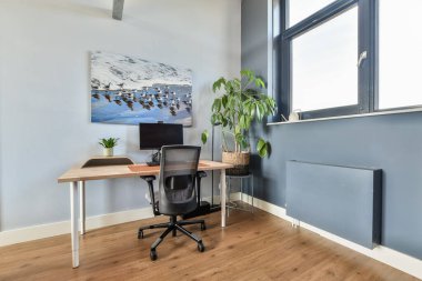 Geniş pencereli, parlak, minimalist bir alana kurulmuş masa, bilgisayar ve kapalı alan içeren şık bir ofis..