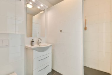 Beyaz duvarları ve döşemeleri olan bir banyo. Duş kabini kapısı arasındaki köşede lavabo da dahil.