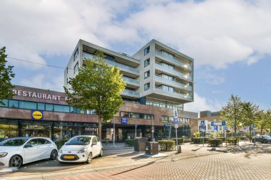 Şık bir bina, restoran tabelası ve kalabalık bir caddenin yakınına park edilmiş araçların yer aldığı çağdaş bir şehir manzarası..