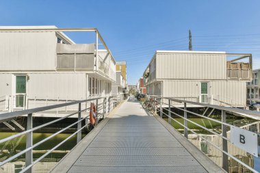 Yürüme yolu ile birbirine bağlı modern yüzen evlerin manzarası, suyla çevrili yenilikçi mimariyi yansıtıyor.