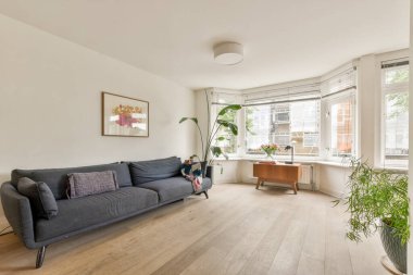 Minimalist dekorun yer aldığı geniş bir oturma odası, doğal ışığa izin veren büyük pencereler, ve rahat bir kanepe, huzurlu bir atmosfer yaratıyor..