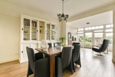 Ahşap bir masa, siyah sandalyeler ve parlak bir pencerenin bulunduğu şık bir yemek salonu, zarif bir dekorla tamamlanmış doğal ışığın atmosferi geliştirmesine olanak sağlıyor..