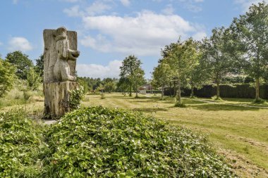 Çarpıcı ahşap bir heykel, ağaçlar ve manikürlü çimlerle çevrili yeşil bir arazinin ortasında, doğal güzelliği ve sanatsallığı gözler önüne seriyor..