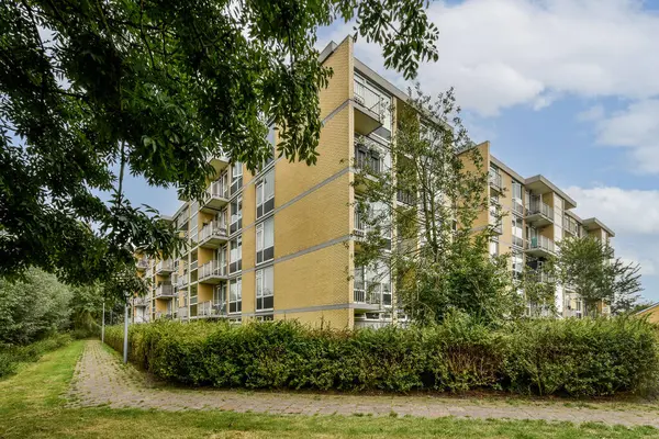 Yeşillik ağaçlar ve çalıların arasına yerleşmiş modern bir apartman kompleksi barındıran çağdaş yerleşim mimarisi, doğayla uyumlu kentsel yaşamı vurguluyor..