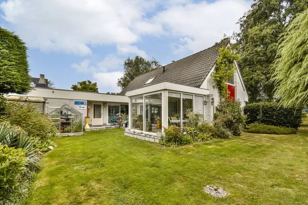 Geniş cam pencereli modern bir ev canlı yeşil bir bahçenin ortasında, mimari ve doğanın bir karışımını sergiliyor..