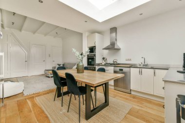 Çağdaş bir mutfak, şık bir yemek masası ve yukarıdaki tavan penceresinden gelen doğal ışıkla parlayan şık sandalyeler. Temiz çizgiler ve minimalist tasarım alanı geliştirir.