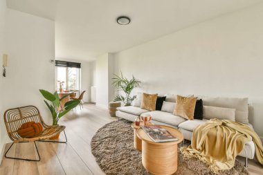 Rahat mobilyaların, yumuşak dokuların ve doğal ışığın bulunduğu sakin, modern bir oturma odası, dinlenmek için sıcak bir davet atmosferi yaratıyor..